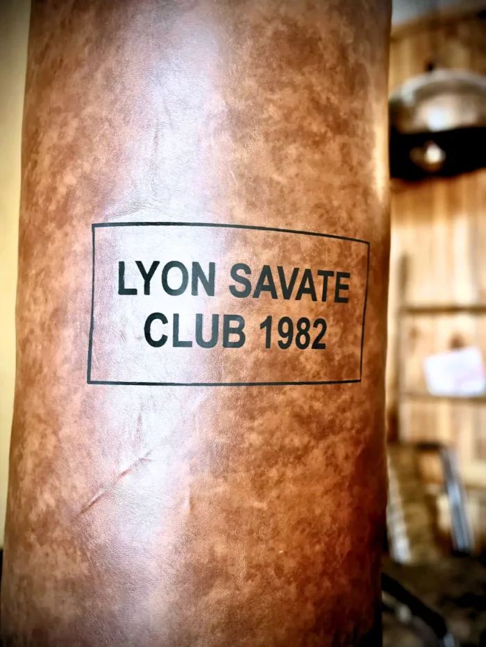 Un sac de frappe old school avec l'inscription "Lyon savate club 1982"