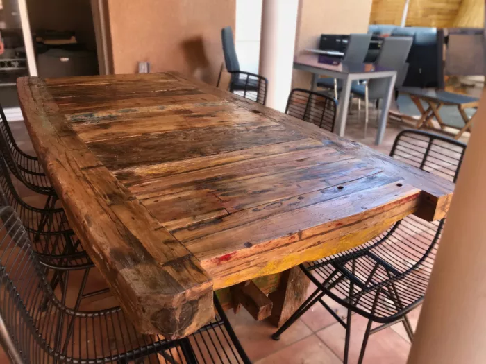 Une terrasse avec une table en vieux bois et des chaises en métal noir