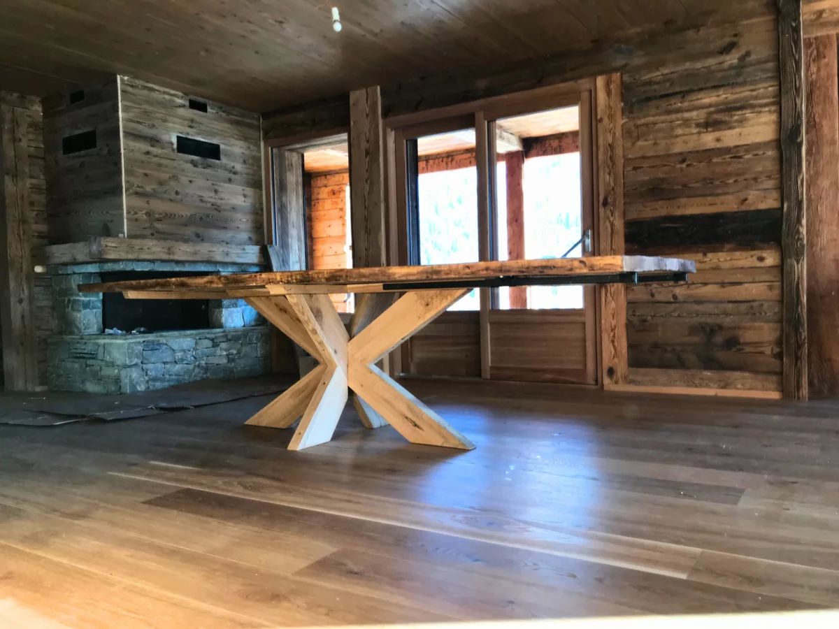 Un salon d'un chalet tout en bois, avec une cheminée en pierre, et une table tout en bois, avec pied de table central en chêne massif